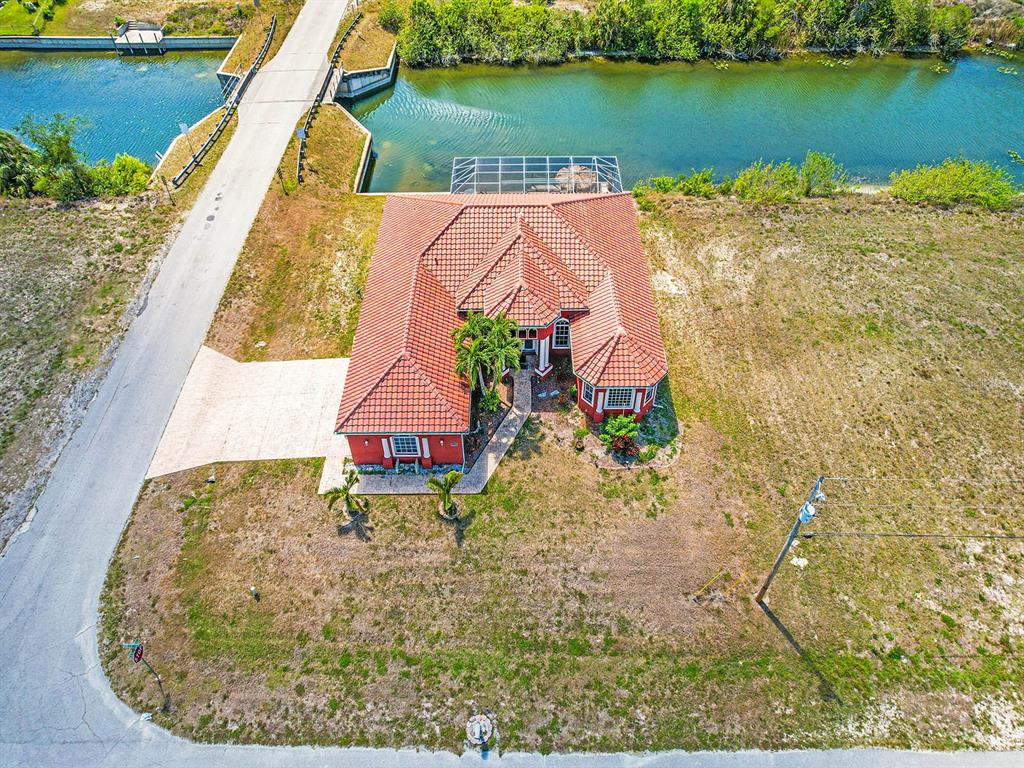 An aerial view shows a red-roofed house with a pool cage beside a canal — 1112 NW 9TH AVENUE, CAPE CORAL, FL