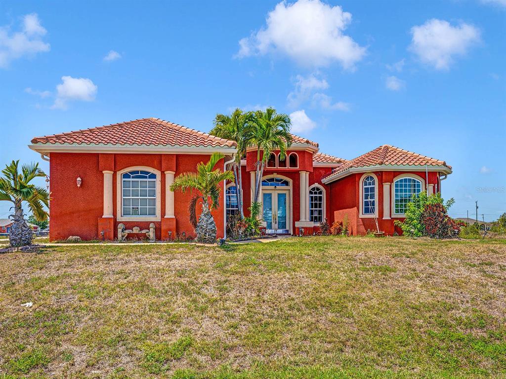A single-story red stucco house with a tiled roof and arched windows under a blue sky — 1112 NW 9TH AVENUE, CAPE CORAL, FL