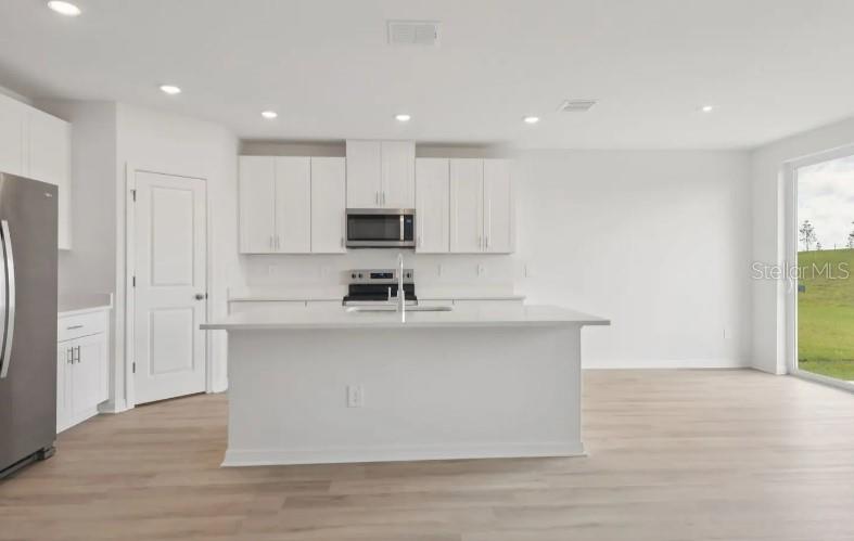A modern kitchen features white cabinets, stainless steel appliances, a center island, and light flooring — 12562 HOURGLASS WAY, DADE CITY, FL