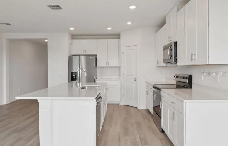 A modern kitchen features white cabinets, stainless steel appliances, and a large central island — 12562 HOURGLASS WAY, DADE CITY, FL