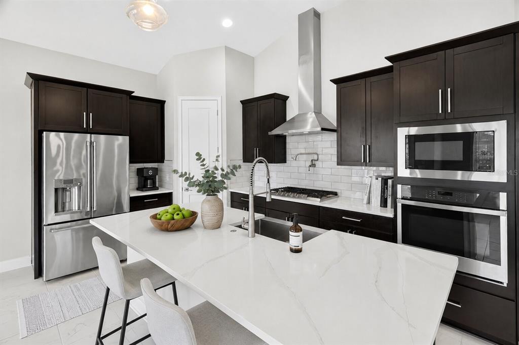 A modern kitchen features dark wood cabinets, white quartz countertops, and stainless steel appliances — 11943B SW 31ST ROAD, GAINESVILLE, FL
