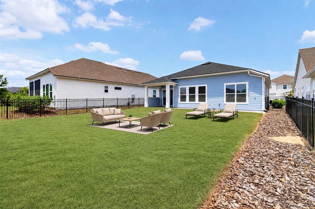 A backyard with a blue house, a patio set on a rug, and a gravel path — 11943B SW 31ST ROAD, GAINESVILLE, FL
