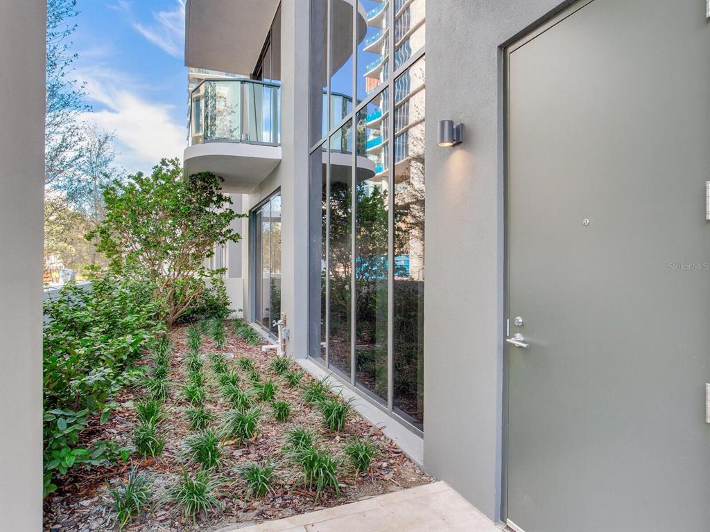A gray exterior door sits beside a large glass window wall and a landscaped garden — 3020 W SANTIAGO STREET UNIT 4, TAMPA, FL