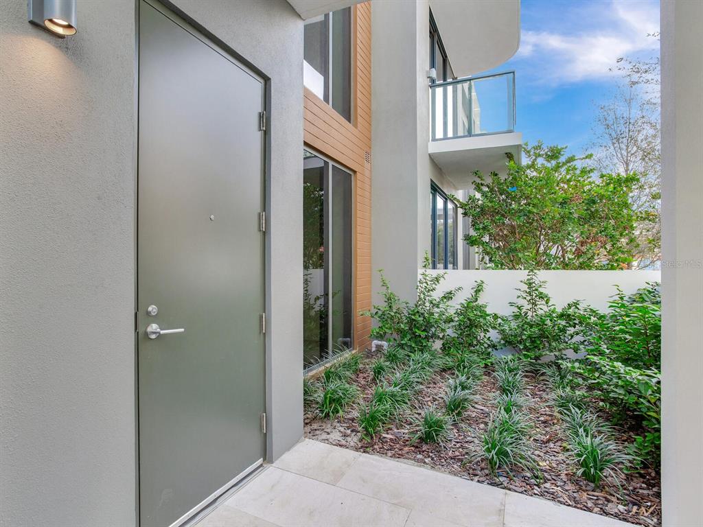 A modern exterior entrance features a gray door, large windows, and a landscaped garden bed — 3020 W SANTIAGO STREET UNIT 4, TAMPA, FL