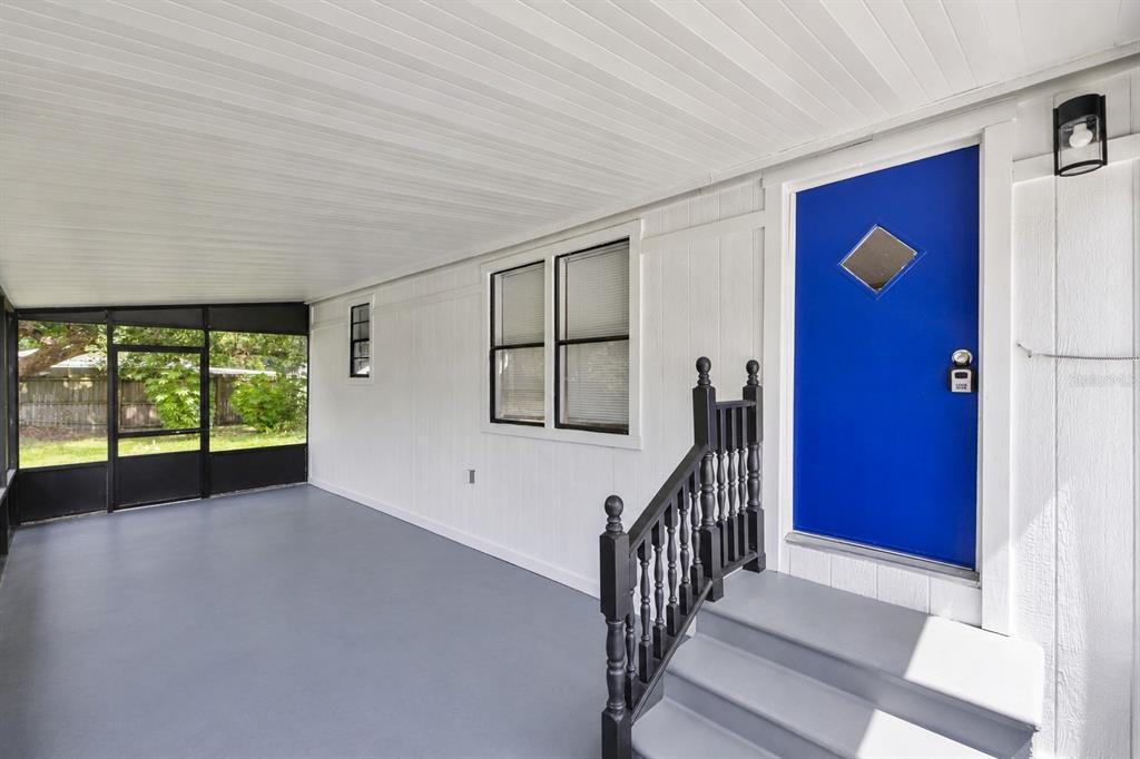 A covered porch features gray flooring, white siding, black railings, and a bright blue door — 1706 CHARLESTON LANE, ST CLOUD, FL