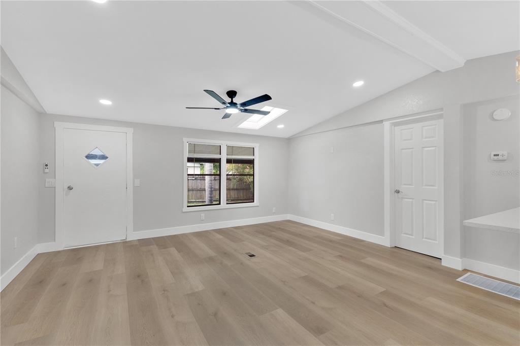 A bright living room features light wood-look flooring, white walls, a ceiling fan, and a window — 1706 CHARLESTON LANE, ST CLOUD, FL