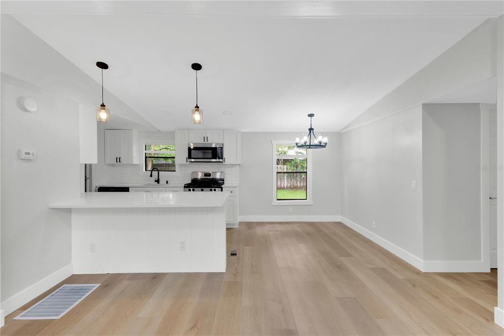 A bright, open-concept kitchen and dining area features white cabinetry, quartz countertops, and light wood flooring — 1706 CHARLESTON LANE, ST CLOUD, FL