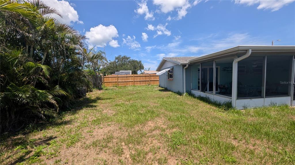 A grassy backyard features a screened-in porch attached to a house and a wooden fence — 3452 CHAUNCY ROAD, HOLIDAY, FL