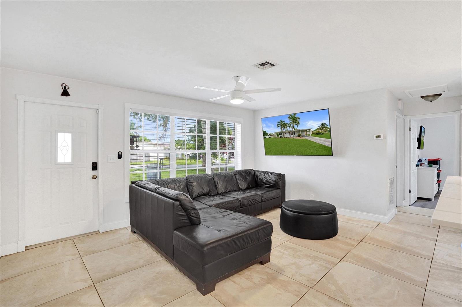A living room features a black sectional sofa, a round ottoman, and a wall-mounted television — 6298 NW 15th Street, Margate FL 33063, MARGATE, FL