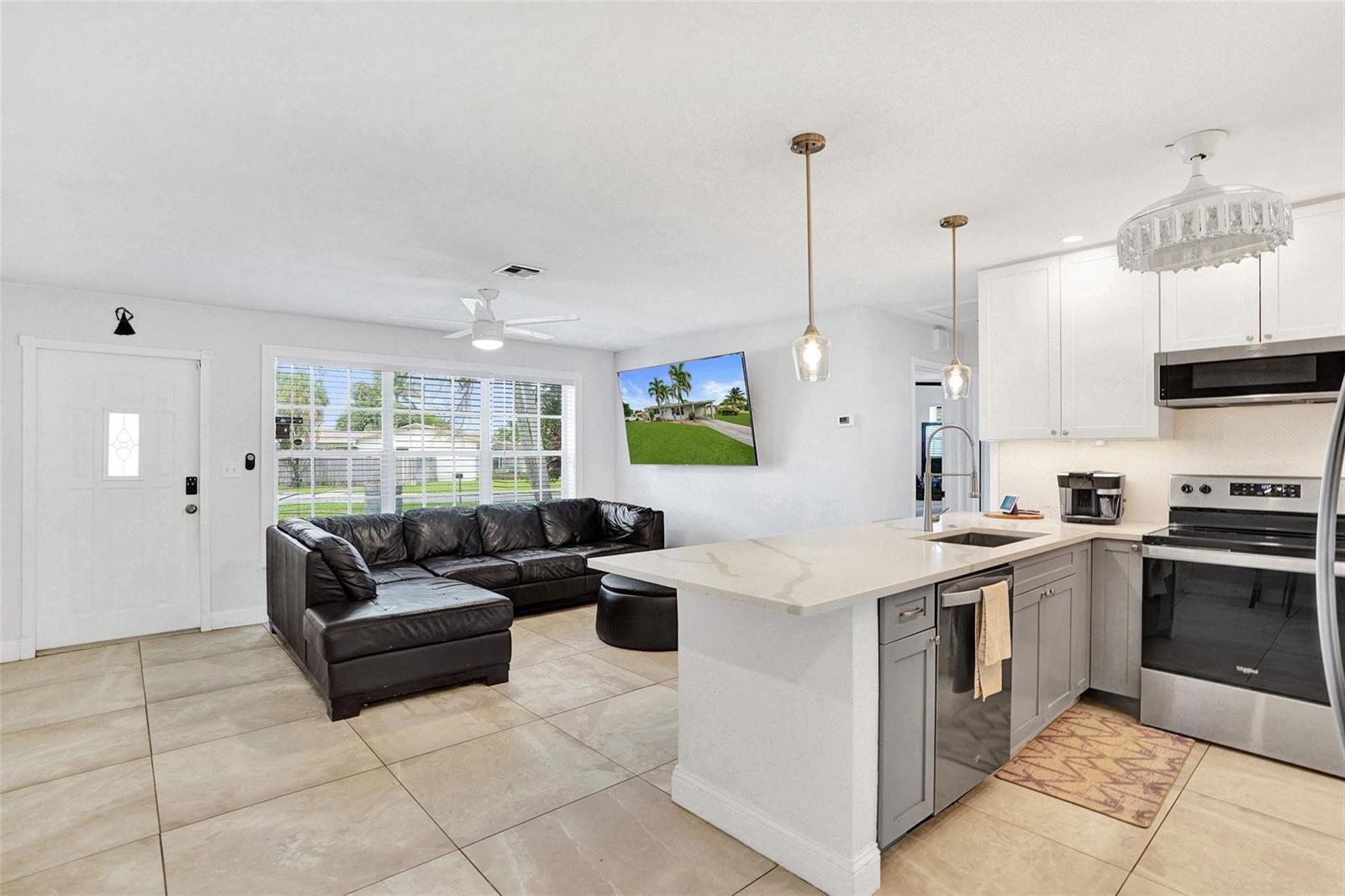 An open-concept kitchen and living area features a black sectional sofa and gray cabinetry — 6298 NW 15th Street, Margate FL 33063, MARGATE, FL