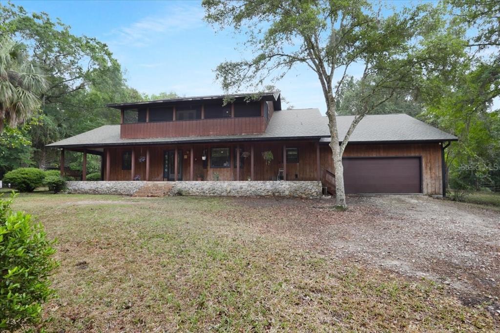 A two-story wood-sided house features a stone foundation, a wrap-around porch, and a garage — 22731 NW 91ST COURT ROAD, MICANOPY, FL