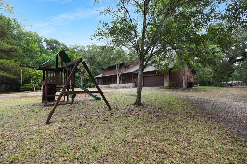 A wooden house features a second-story deck with stairs, a stone chimney, and a swimming pool — 22731 NW 91ST COURT ROAD, MICANOPY, FL