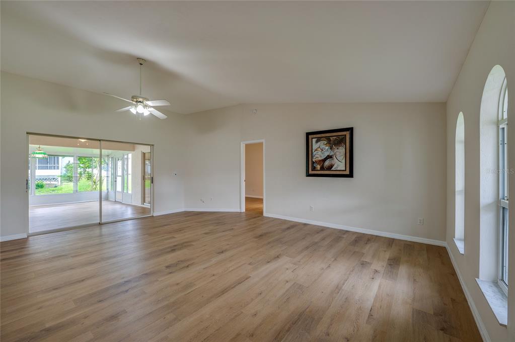A living room with light wood-look flooring, vaulted ceilings, a ceiling fan, and sliding doors — 5450 LANDIS AVENUE, PORT ORANGE, FL