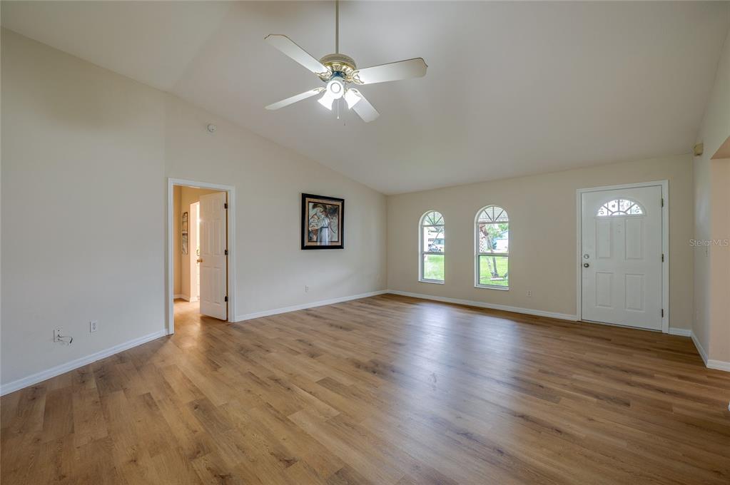 An empty living room with vaulted ceilings, wood-look flooring, a ceiling fan, and two windows — 5450 LANDIS AVENUE, PORT ORANGE, FL