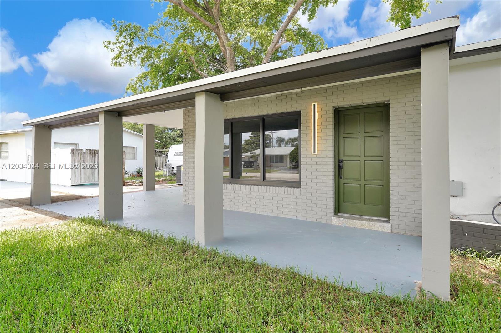 A gray brick house exterior features a covered porch, green door, and large window — 3140 NE 9th Ter, Pompano Beach FL 33064, POMPANO BEACH, FL