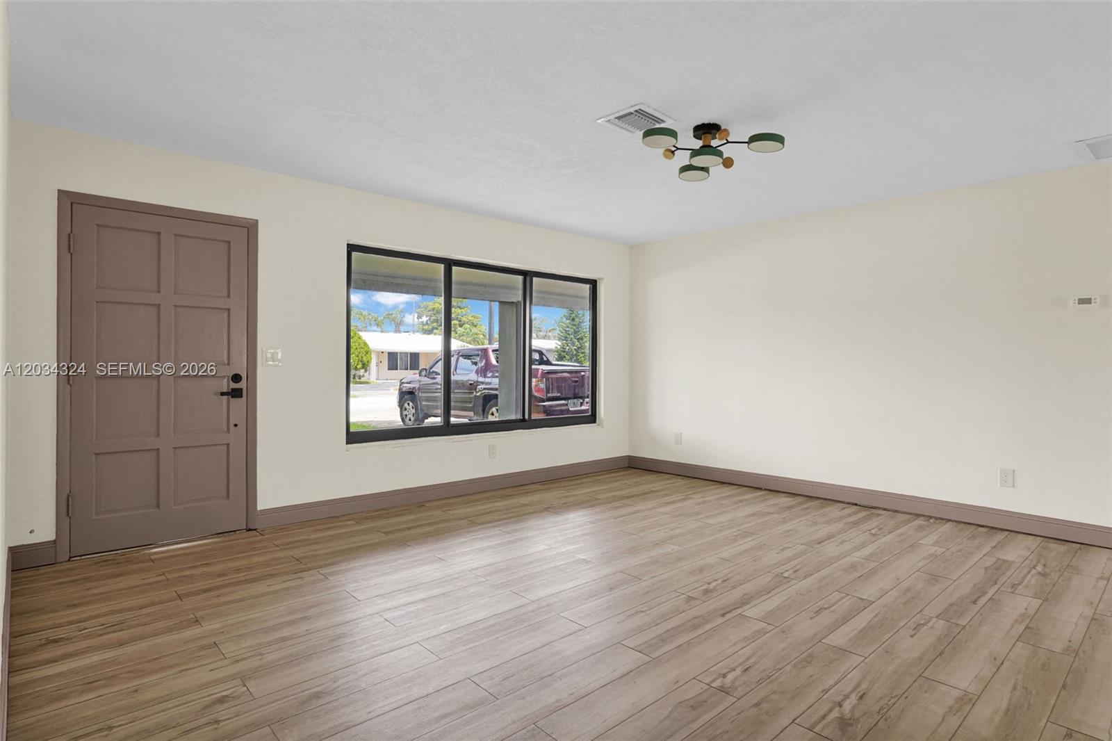 An empty room features light wood-look flooring, cream walls, a dark door, and a ceiling light — 3140 NE 9th Ter, Pompano Beach FL 33064, POMPANO BEACH, FL