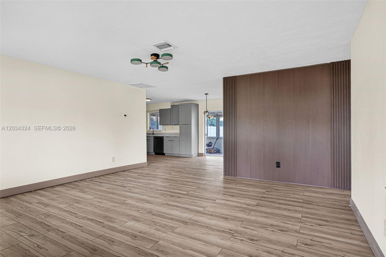 An open-concept living area features wood-look flooring, a paneled accent wall, and a kitchen — 3140 NE 9th Ter, Pompano Beach FL 33064, POMPANO BEACH, FL