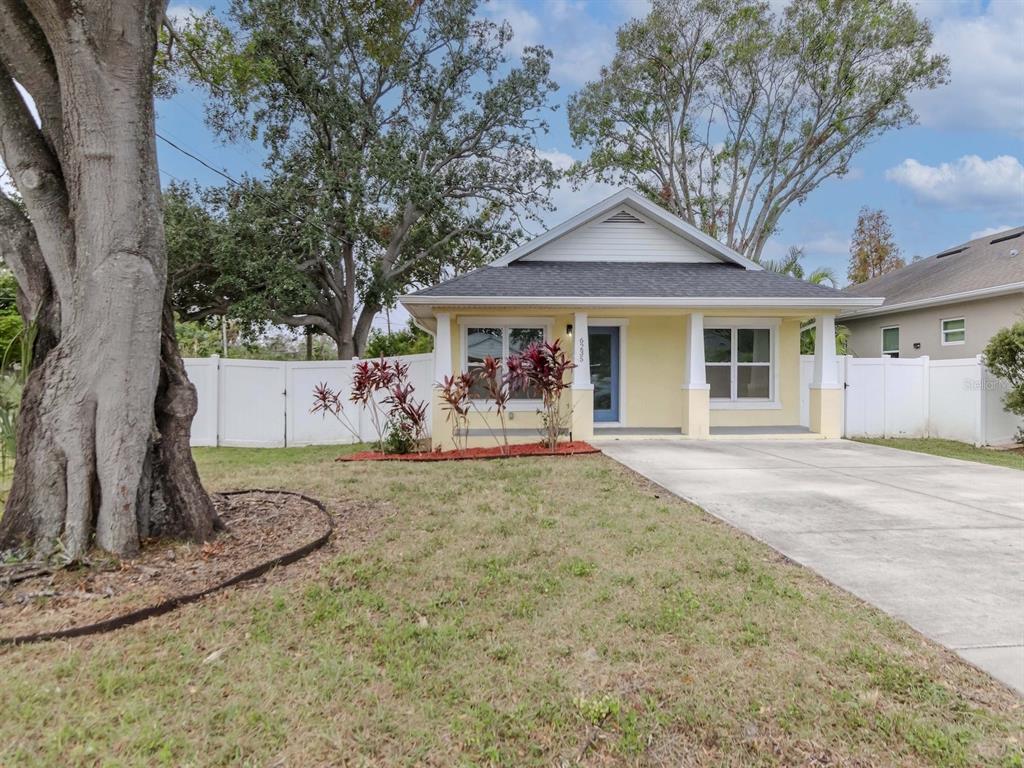 A yellow single-story house with a front porch, concrete driveway, and white vinyl fence — 6235 S ADELIA AVENUE, TAMPA, FL