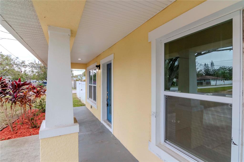 A yellow house exterior features a covered front porch with a blue door and window — 6235 S ADELIA AVENUE, TAMPA, FL