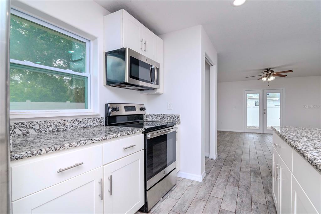 A kitchen with white cabinets, granite countertops, stainless steel appliances, and wood-look tile flooring — 6235 S ADELIA AVENUE, TAMPA, FL