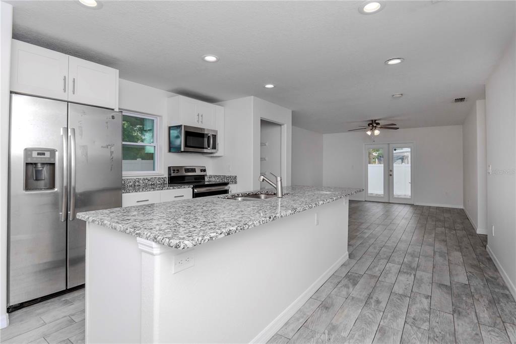 A modern kitchen features white cabinets, granite countertops, a center island, and stainless steel appliances — 6235 S ADELIA AVENUE, TAMPA, FL