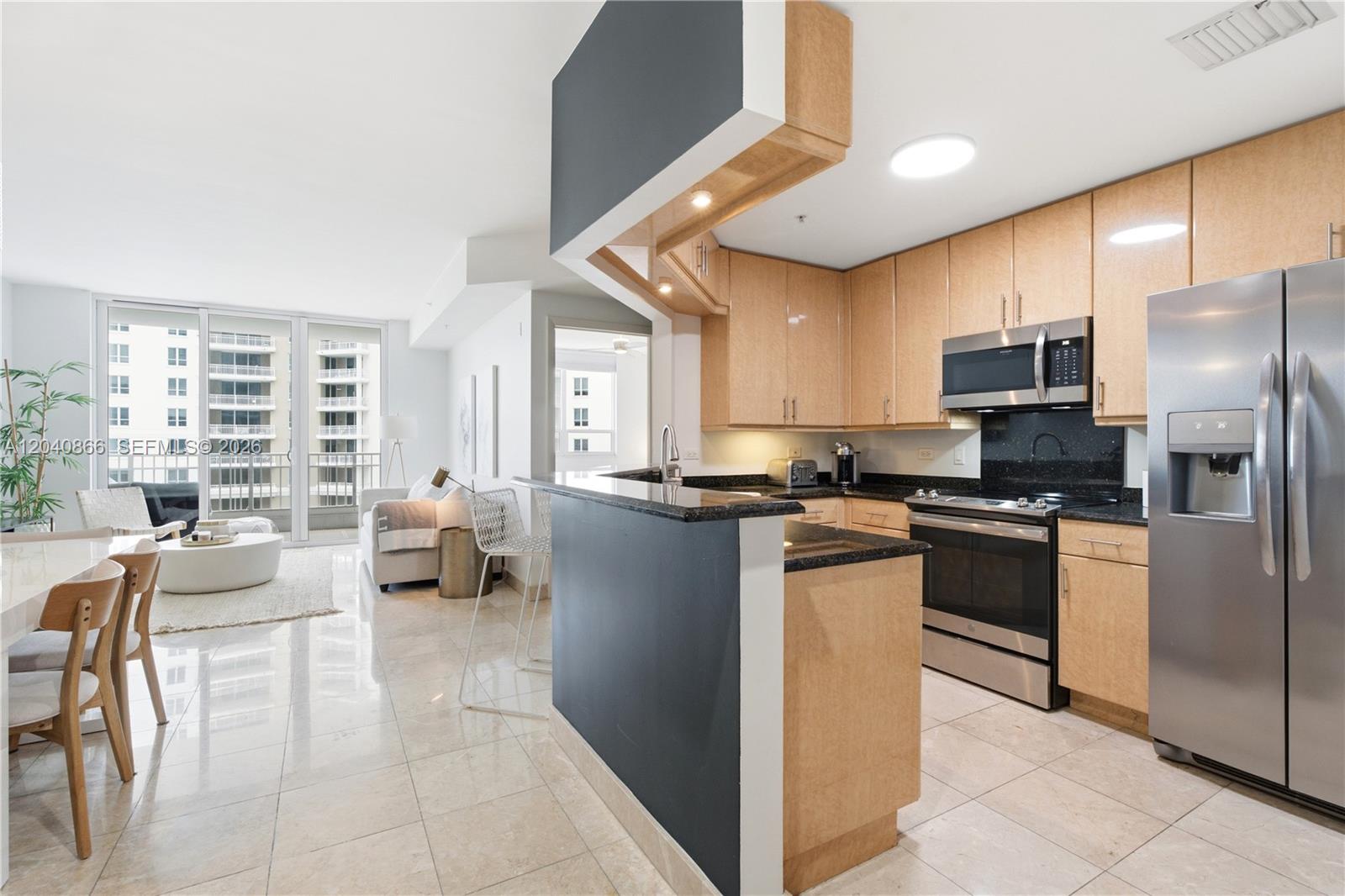 A kitchen with light wood cabinets and black countertops opens to a bright living area — 801 Brickell Key Blvd # 707, Miami FL 33131, MIAMI, FL