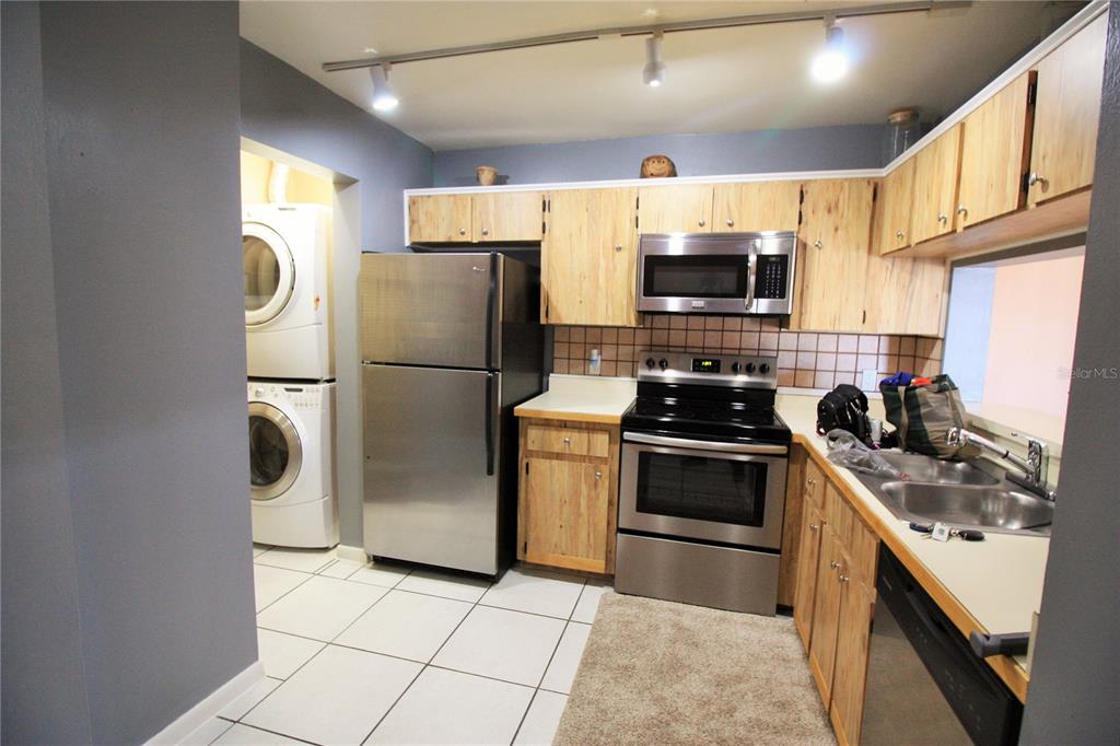 A kitchen features light wood cabinets, stainless steel appliances, and a stacked washer and dryer — 5208 VIA HACIENDA CIRCLE UNIT A201, ORLANDO, FL