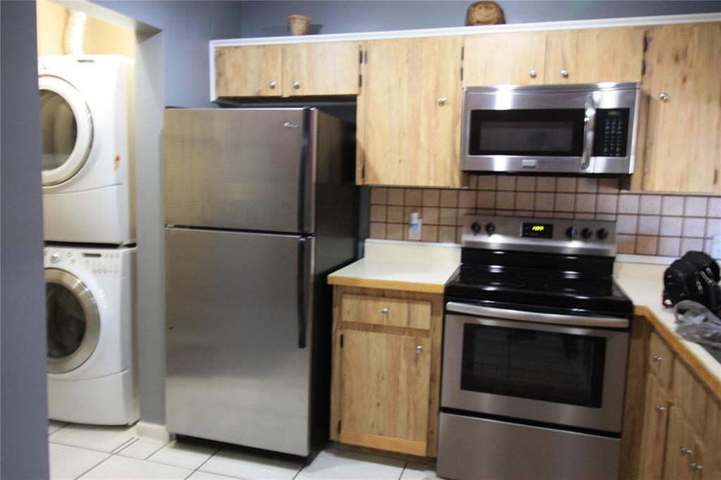 A kitchen features stainless steel appliances, light wood cabinets, and a stacked washer and dryer — 5208 VIA HACIENDA CIRCLE UNIT A201, ORLANDO, FL