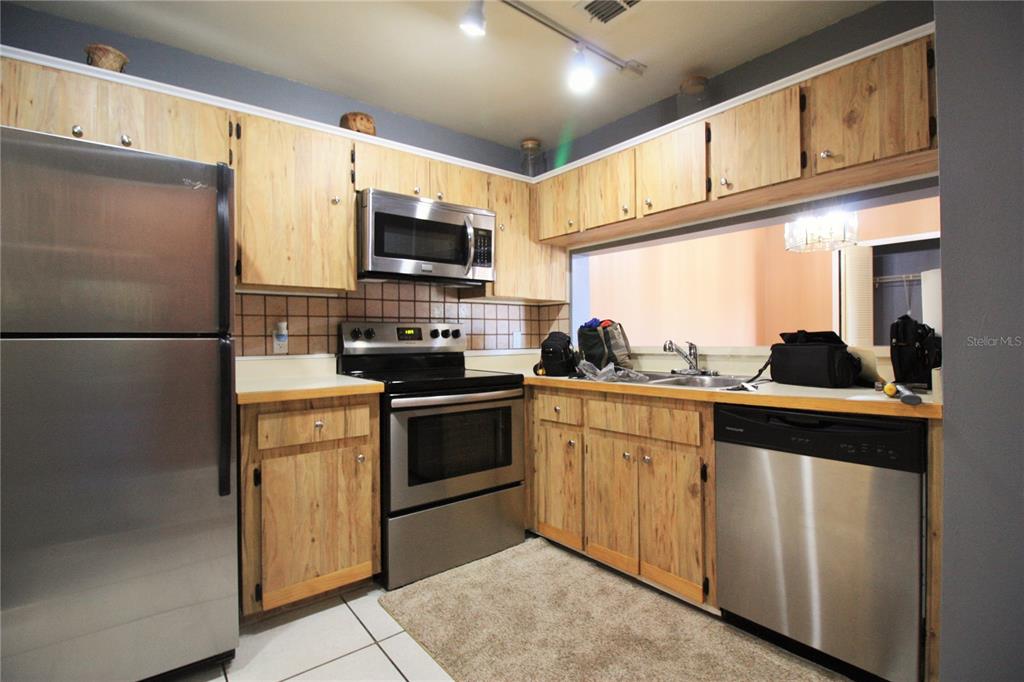 A kitchen with light wood cabinets, stainless steel appliances, and a tiled backsplash — 5208 VIA HACIENDA CIRCLE UNIT A201, ORLANDO, FL
