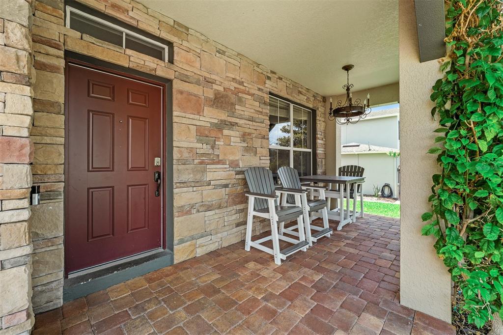 A covered stone-walled porch features a red front door and a small outdoor dining set — 4259 CAPLOCK STREET, CLERMONT, FL