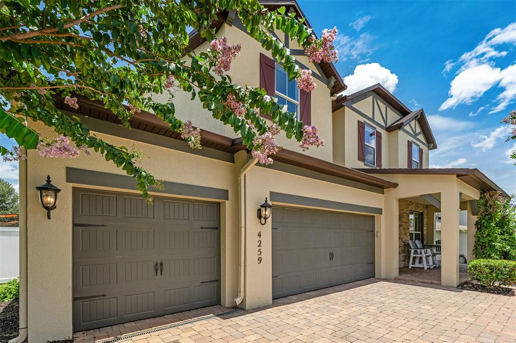 A two-story house exterior features a three-car garage, tan stucco walls, and a brick driveway — 4259 CAPLOCK STREET, CLERMONT, FL