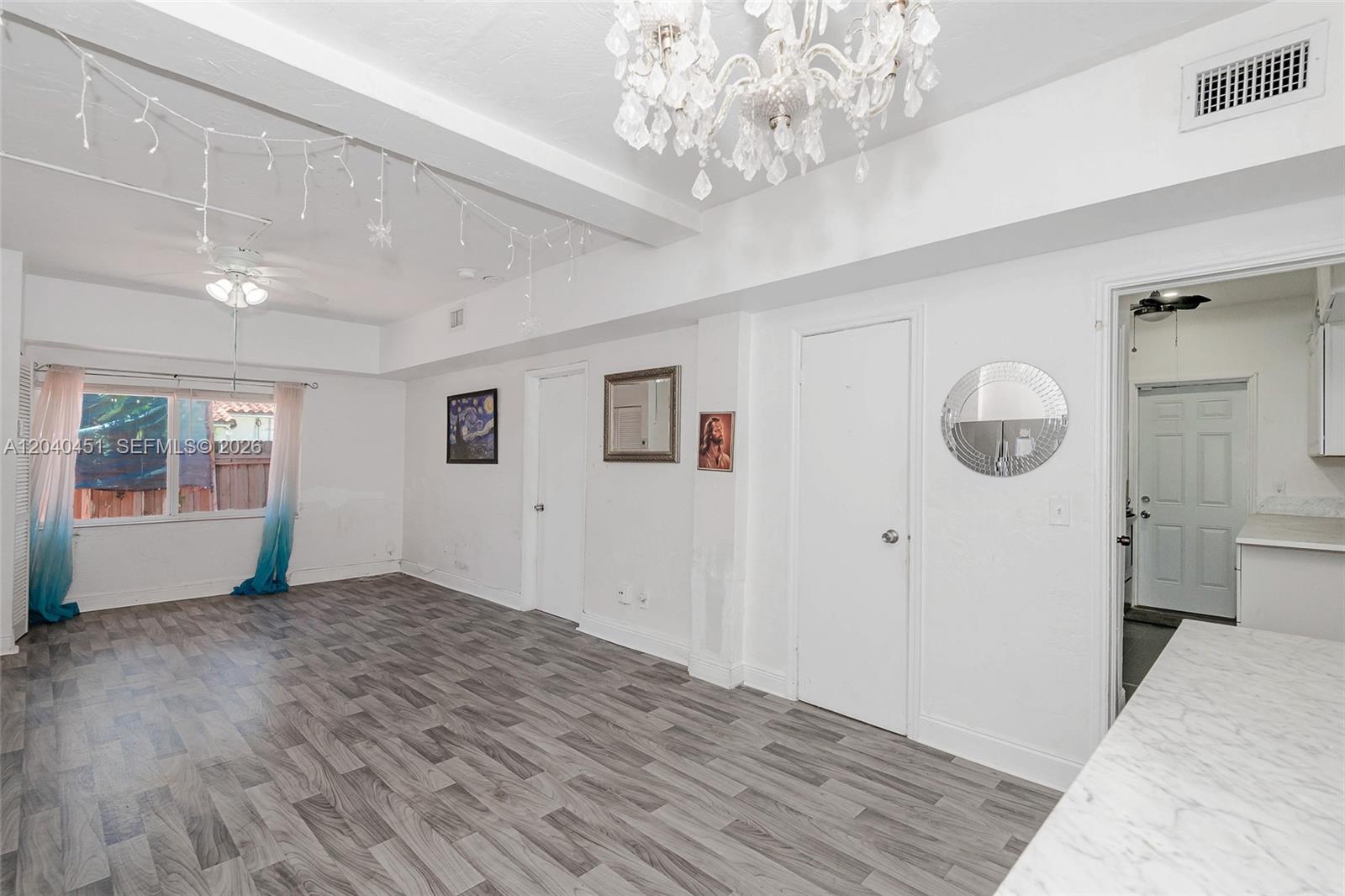 A white-walled room features gray wood-look flooring, a crystal chandelier, and a ceiling fan — 259 NE 111th St, Miami FL 33161, MIAMI, FL