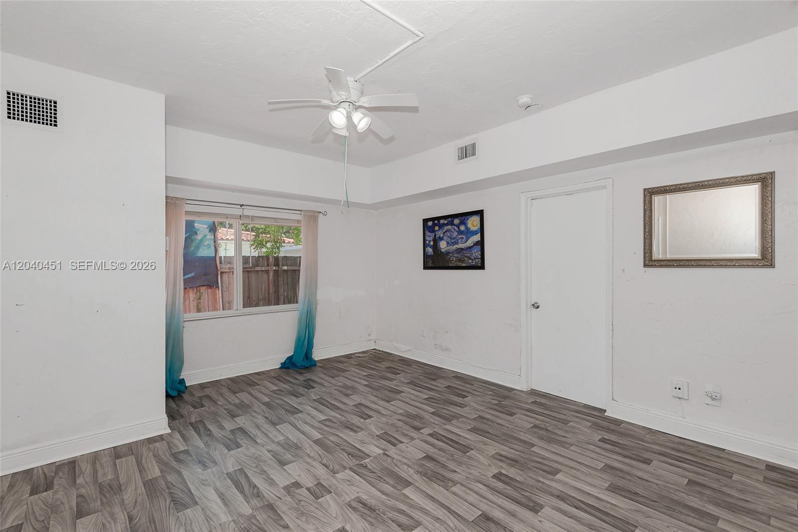 An empty bedroom features white walls, gray wood-look flooring, a ceiling fan, and a window — 259 NE 111th St, Miami FL 33161, MIAMI, FL