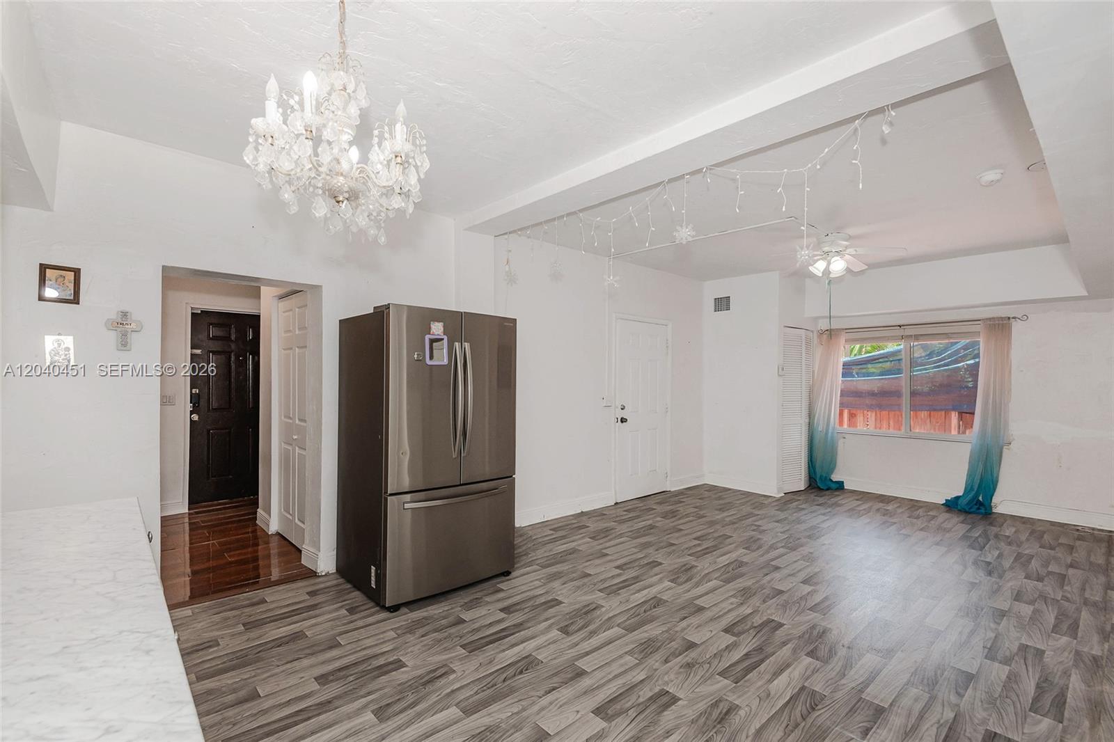 A room with gray wood-look flooring, a stainless steel refrigerator, and a crystal chandelier — 259 NE 111th St, Miami FL 33161, MIAMI, FL