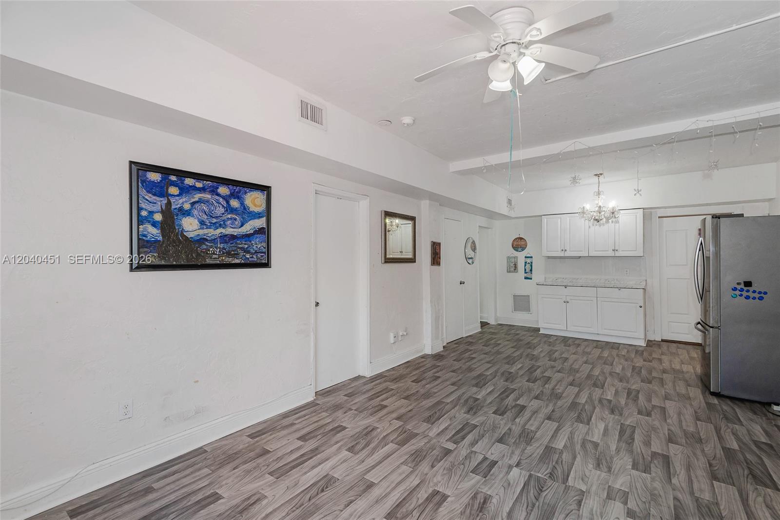 A room with white walls, wood-look flooring, a ceiling fan, and a small kitchen area — 259 NE 111th St, Miami FL 33161, MIAMI, FL