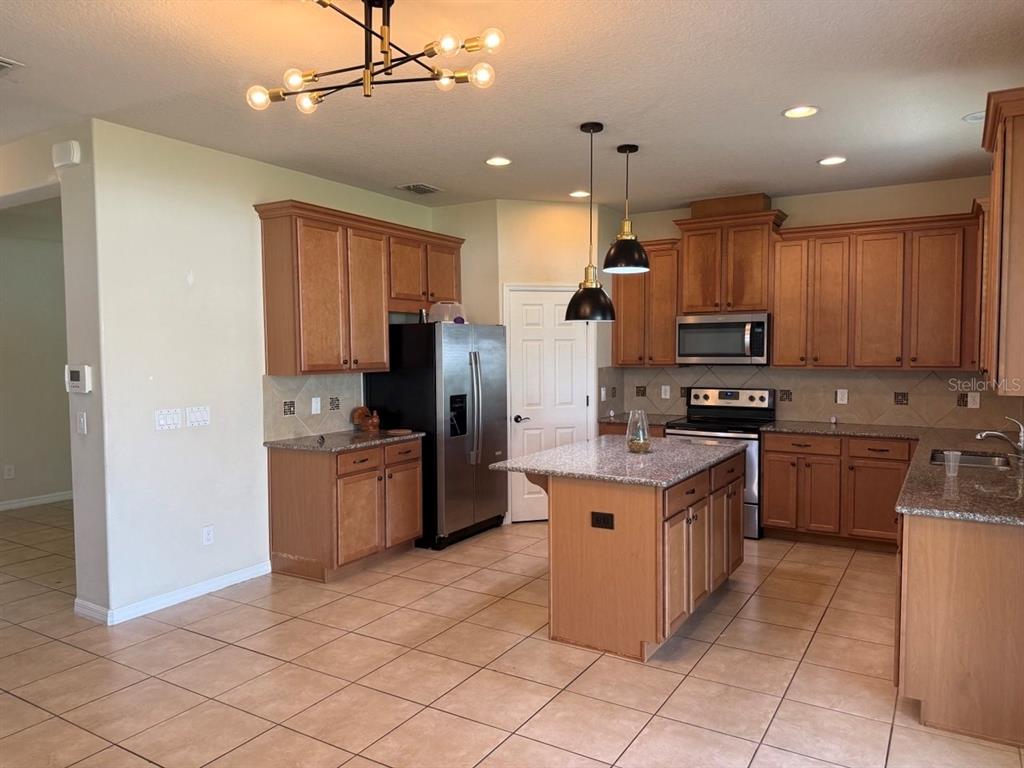 A kitchen with wood cabinets, granite countertops, a center island, and tile flooring — 8026 CORKFIELD AVE, ORLANDO, FL