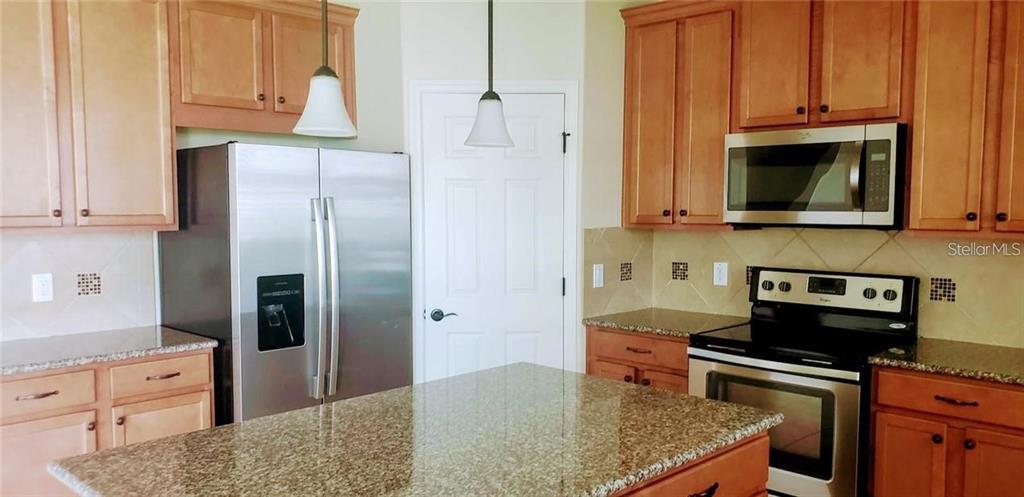 A kitchen features light wood cabinets, stainless steel appliances, and a granite-topped island — 8026 CORKFIELD AVE, ORLANDO, FL