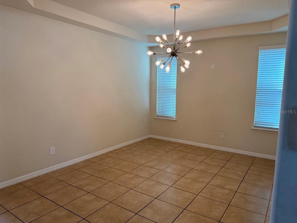 An empty dining room features tan tile flooring, light walls, and a modern sputnik chandelier — 8026 CORKFIELD AVE, ORLANDO, FL