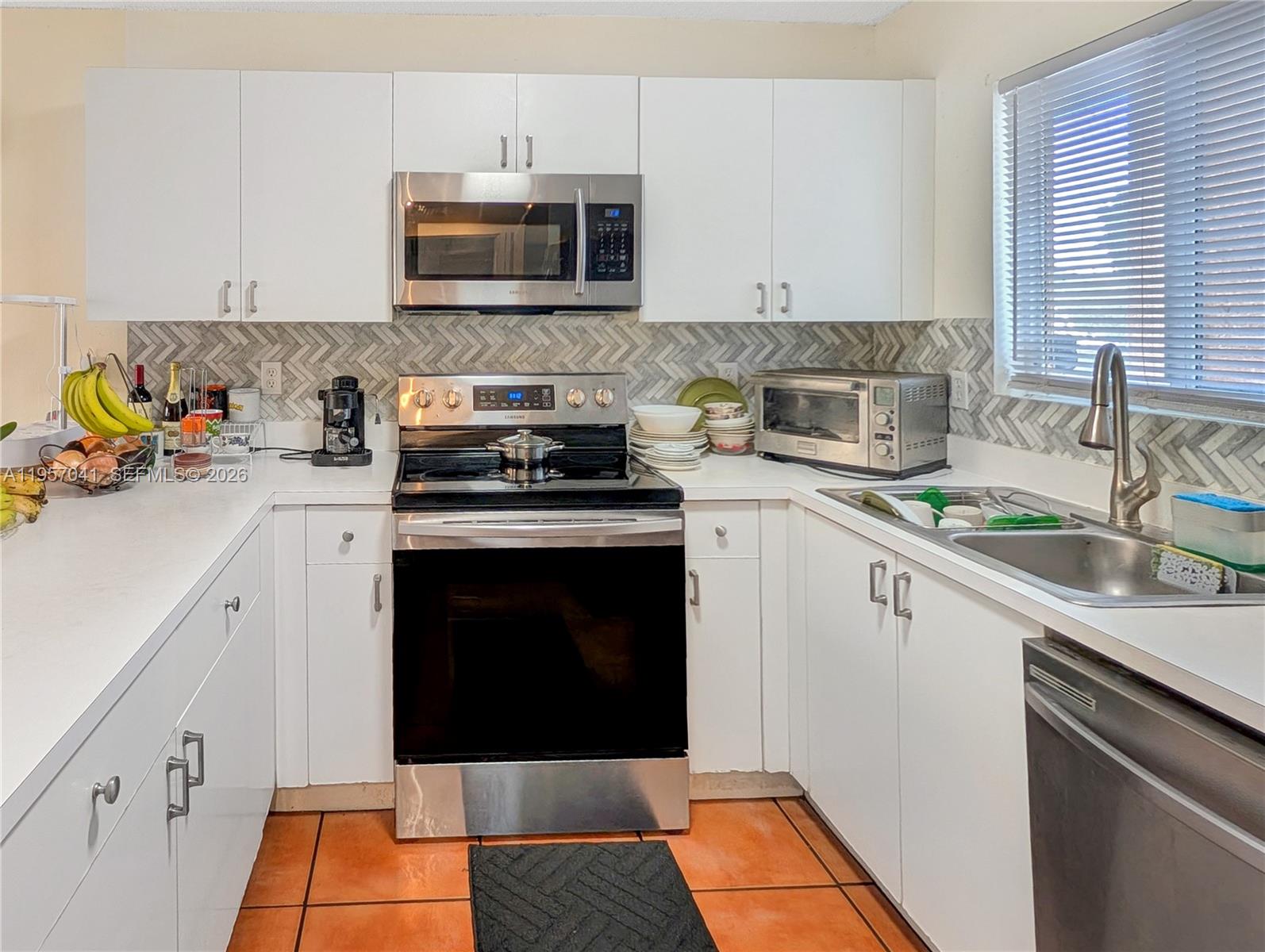 A kitchen features white cabinets, stainless steel appliances, a herringbone backsplash, and orange tile flooring — 6205 Kendale Lakes Cir # 289, Miami FL 33183, MIAMI, FL