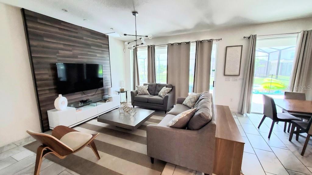 A living room features a wood-paneled accent wall, a television, and neutral-toned furniture — 3810 OAKVILLE AVENUE, KISSIMMEE, FL