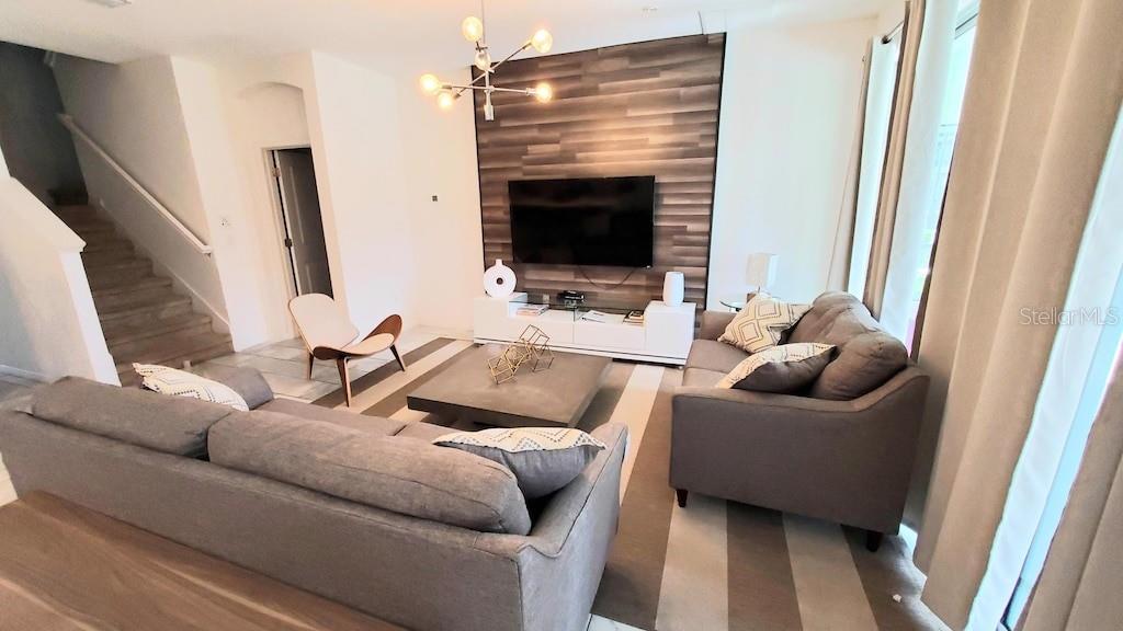 A living room features a wood-paneled accent wall, a television, and two gray sofas — 3810 OAKVILLE AVENUE, KISSIMMEE, FL