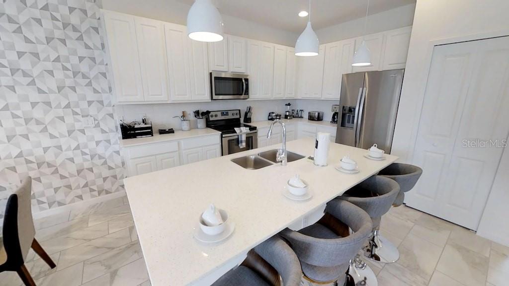 A modern kitchen features white cabinetry, a quartz island with seating, and geometric patterned wallpaper — 3810 OAKVILLE AVENUE, KISSIMMEE, FL