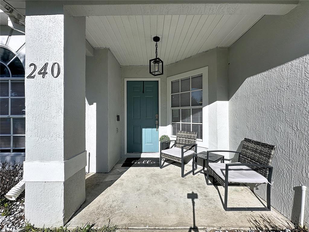 A covered front porch features a teal door, two wicker chairs, and a hanging lantern — 240 SUNRISE RD, DAVENPORT, FL