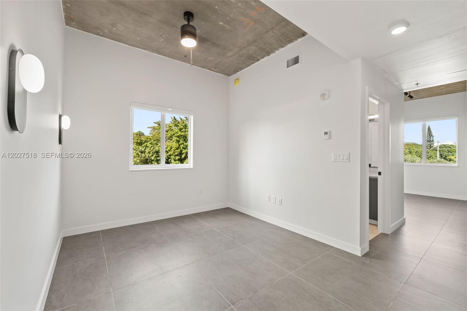 An empty room features gray tile flooring, white walls, and an exposed concrete ceiling — 315 NW 32 ST # 305, Miami FL 33127, MIAMI, FL