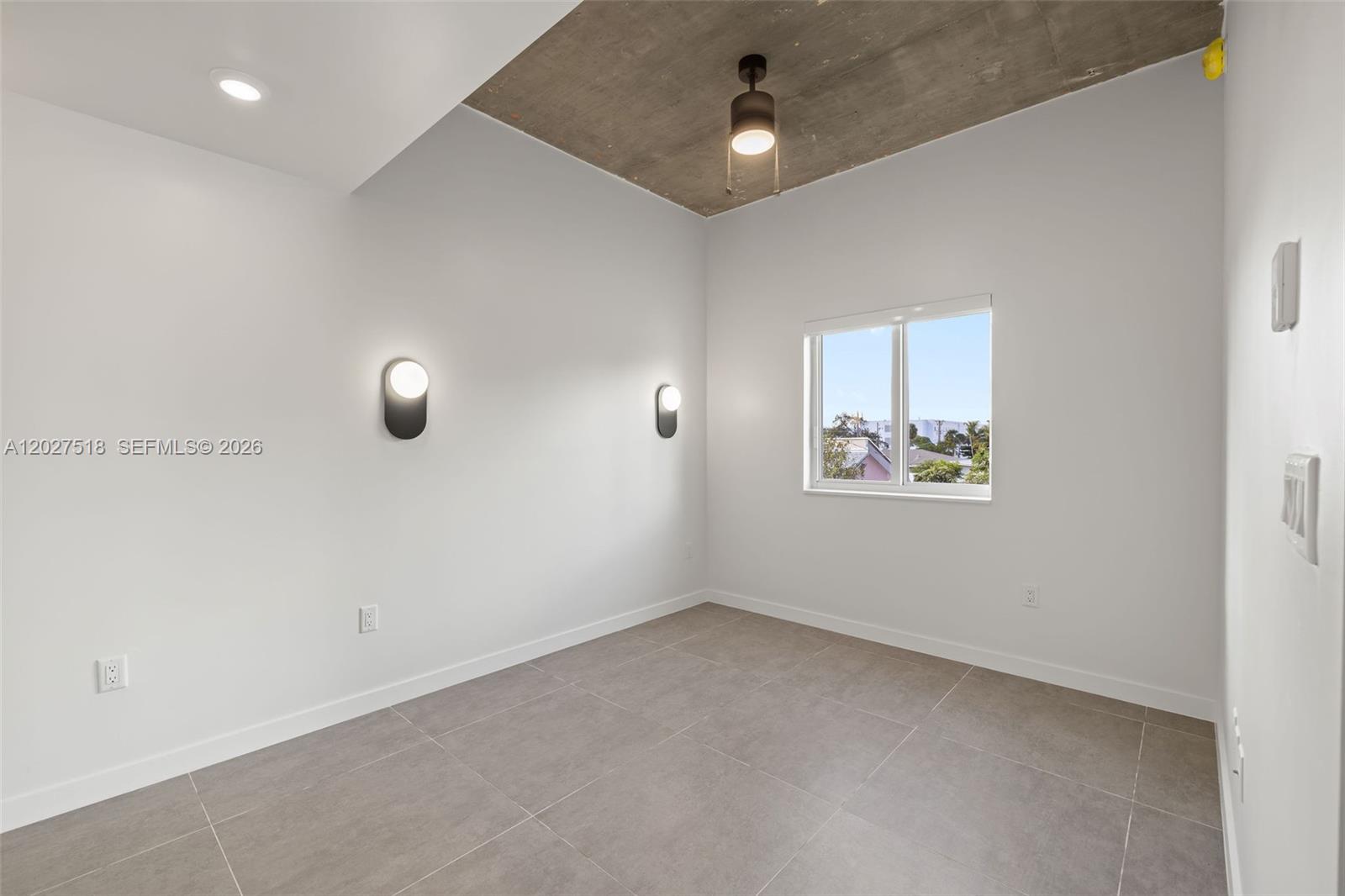 An empty room features a concrete ceiling, gray tile flooring, and modern wall sconces — 315 NW 32 ST # 305, Miami FL 33127, MIAMI, FL