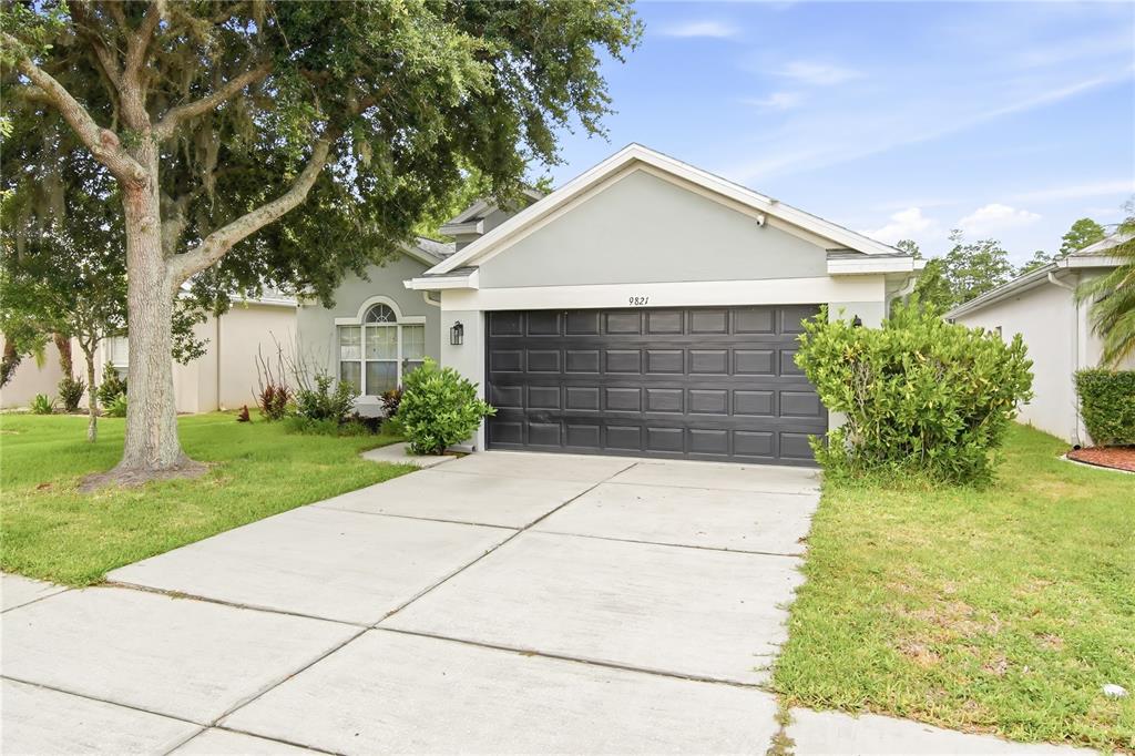 A single-story house with a gray exterior, a dark garage door, and a concrete driveway — 9821 JASMINE BROOK CIRCLE, LAND O LAKES, FL