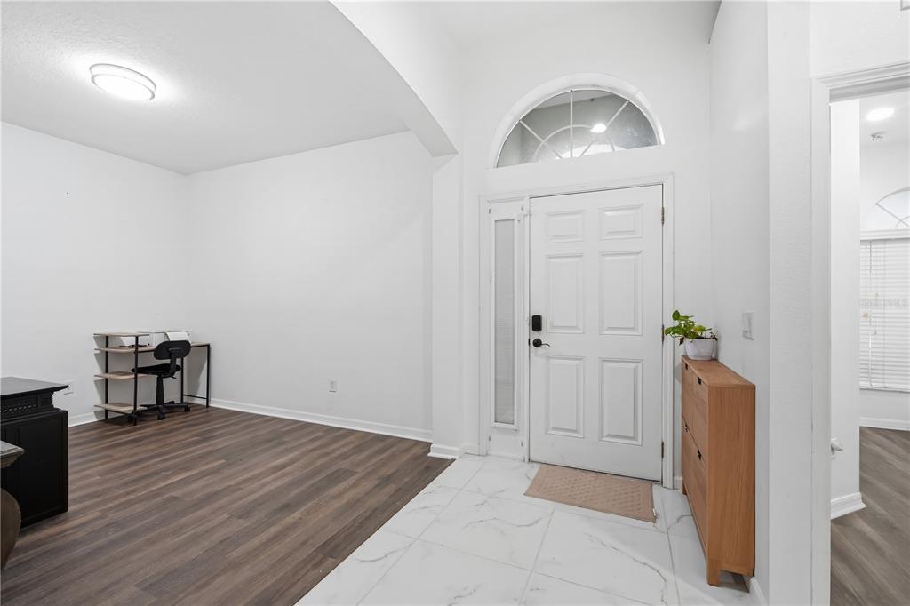 An entryway with white tile floors transitions into a wood-floored room with a home office — 9821 JASMINE BROOK CIRCLE, LAND O LAKES, FL