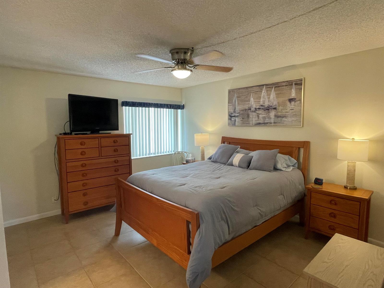 A bedroom features a wooden bed frame, matching dresser, nightstand, and a sailboat wall art piece — 1605 S Us Highway 1, Jupiter FL 33477, JUPITER, FL