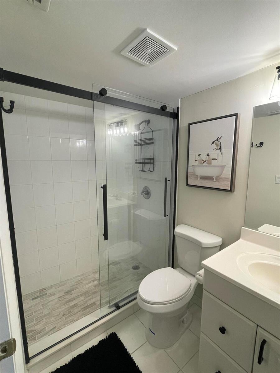 A bathroom features a glass-enclosed walk-in shower, a white toilet, and a vanity with a mirror — 1605 S Us Highway 1, Jupiter FL 33477, JUPITER, FL