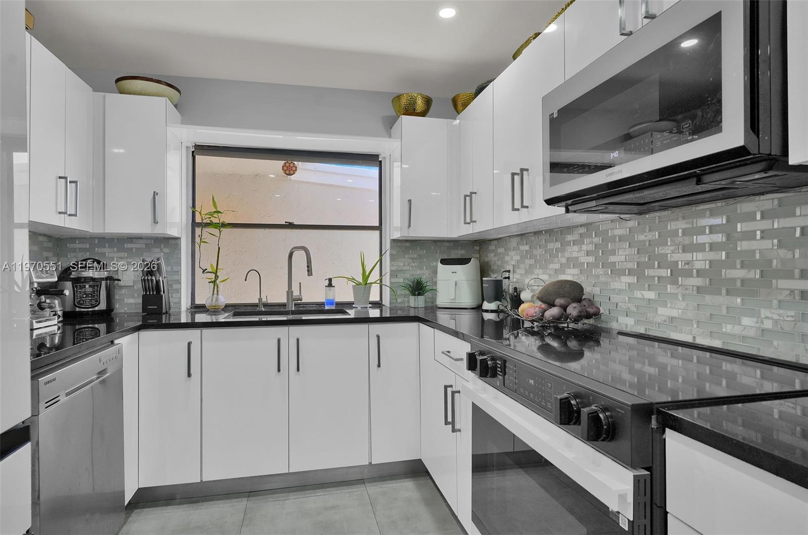 A modern kitchen features white cabinets, black countertops, stainless steel appliances, and a tiled backsplash — 17032 NW 63rd Pl, Hialeah FL 33015, HIALEAH, FL